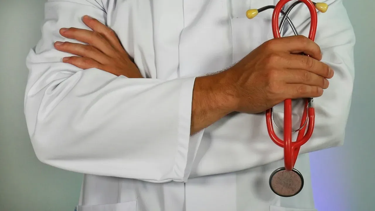 Médico com jaleco segurando um estetoscópio vermelho